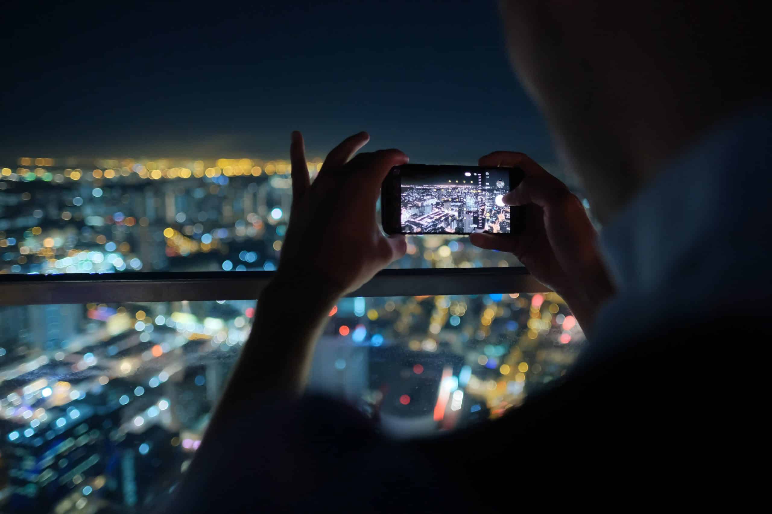 Person taking night cityscape photo with smartphone, representing F3 Private Investigations' surveillance services.