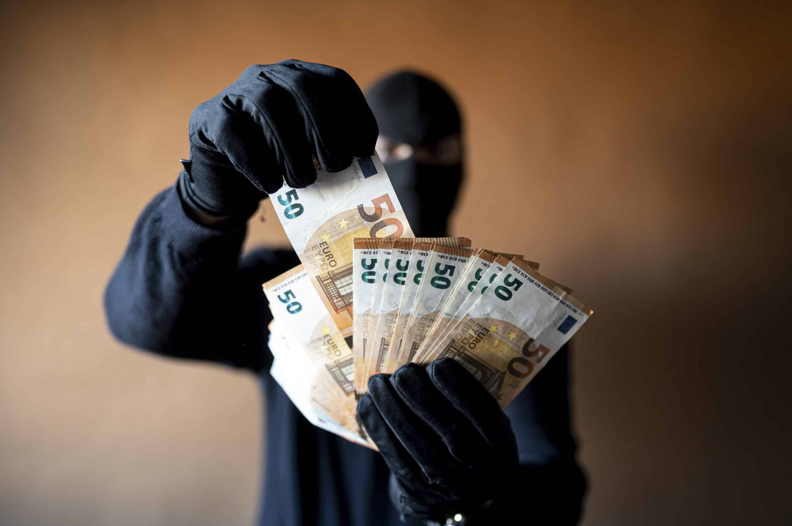 Masked individual holding euro banknotes, emphasizing fraud and theft investigations by F3 Private Investigations.