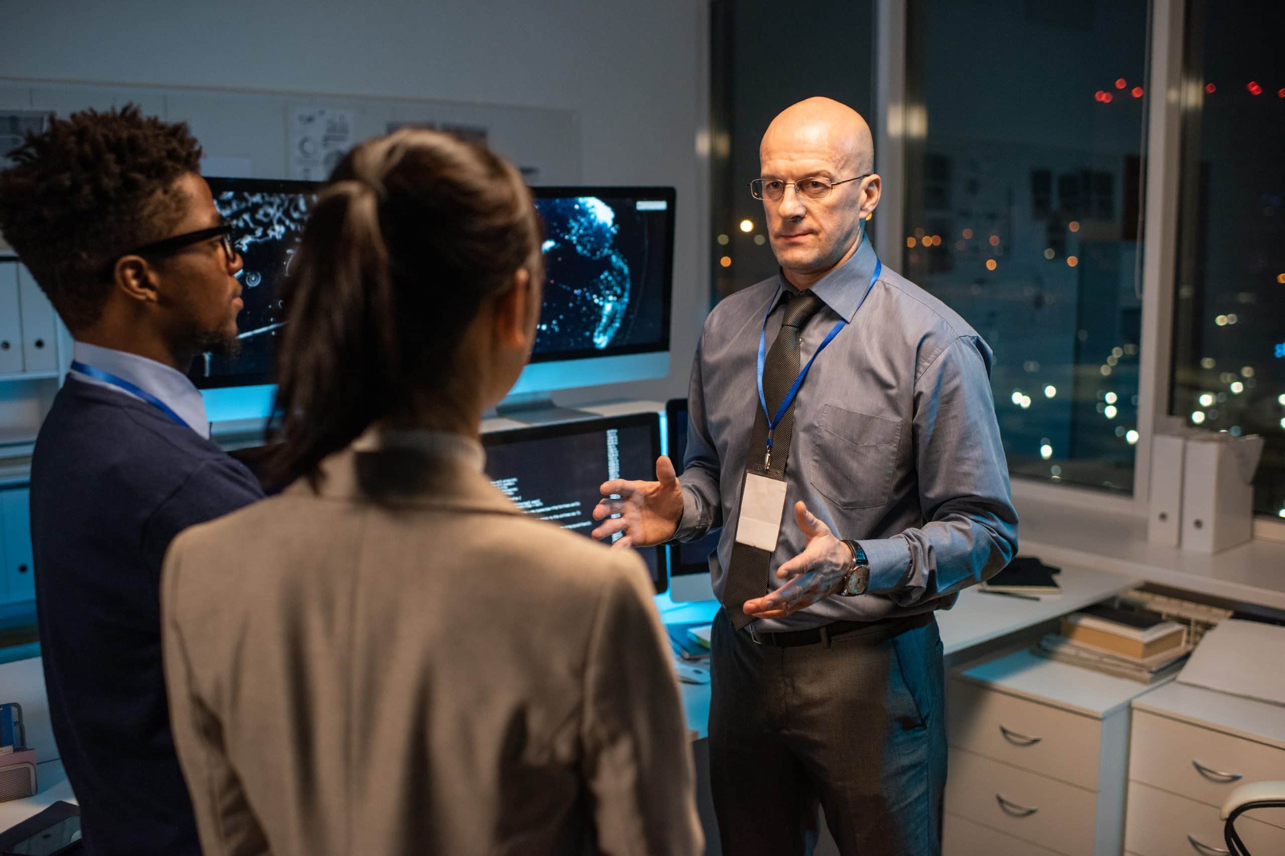 F3 Private Investigations team discussing strategies in a modern office with computer screens displaying digital data.