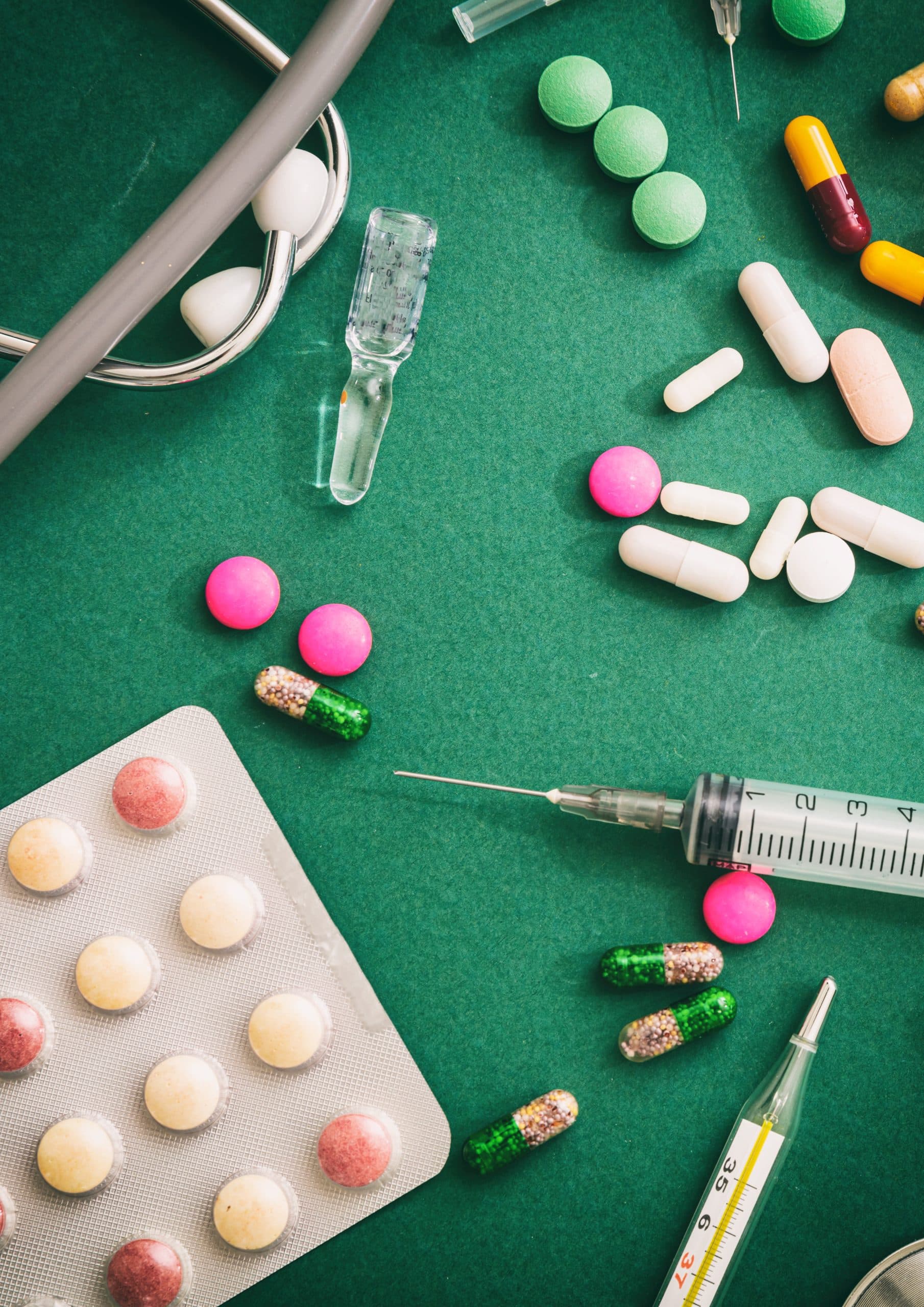 Various pills, syringe, stethoscope on green background.