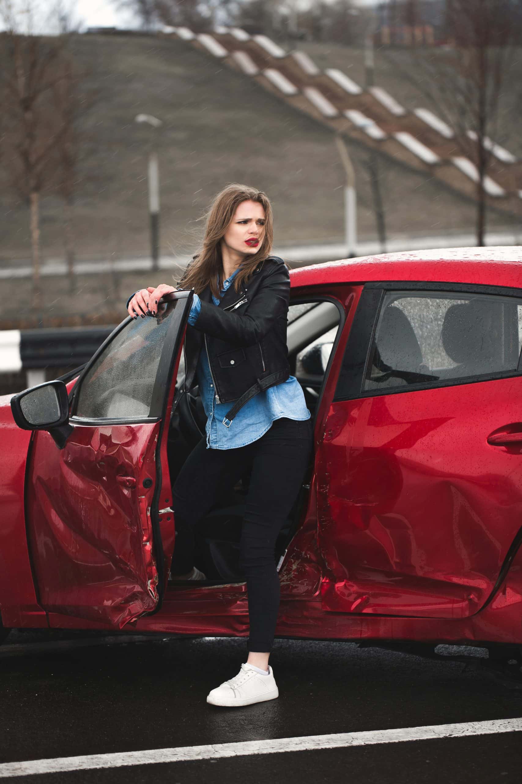 Woman standing by damaged red car