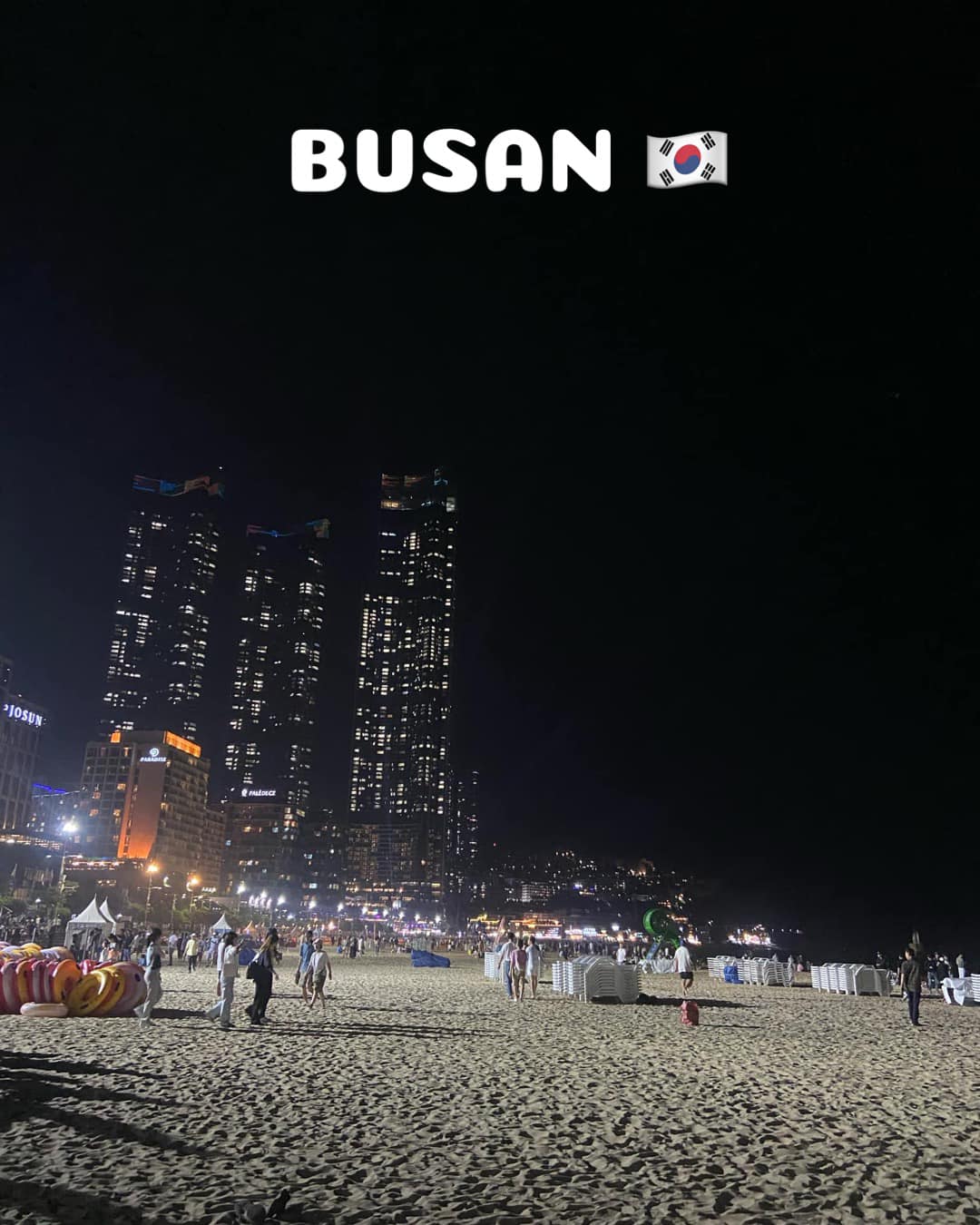 Busan beach at night with skyscraper view.