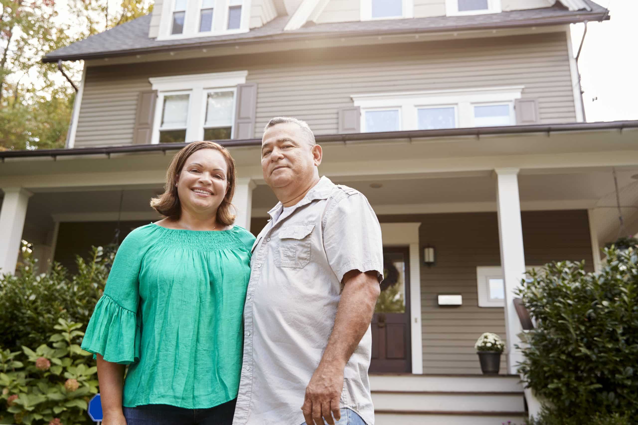 Couple standing outside their house smiling.