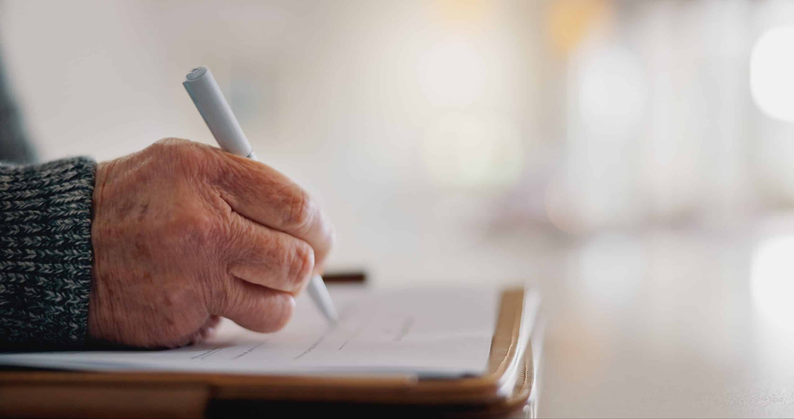 Elderly hand signing document with pen.