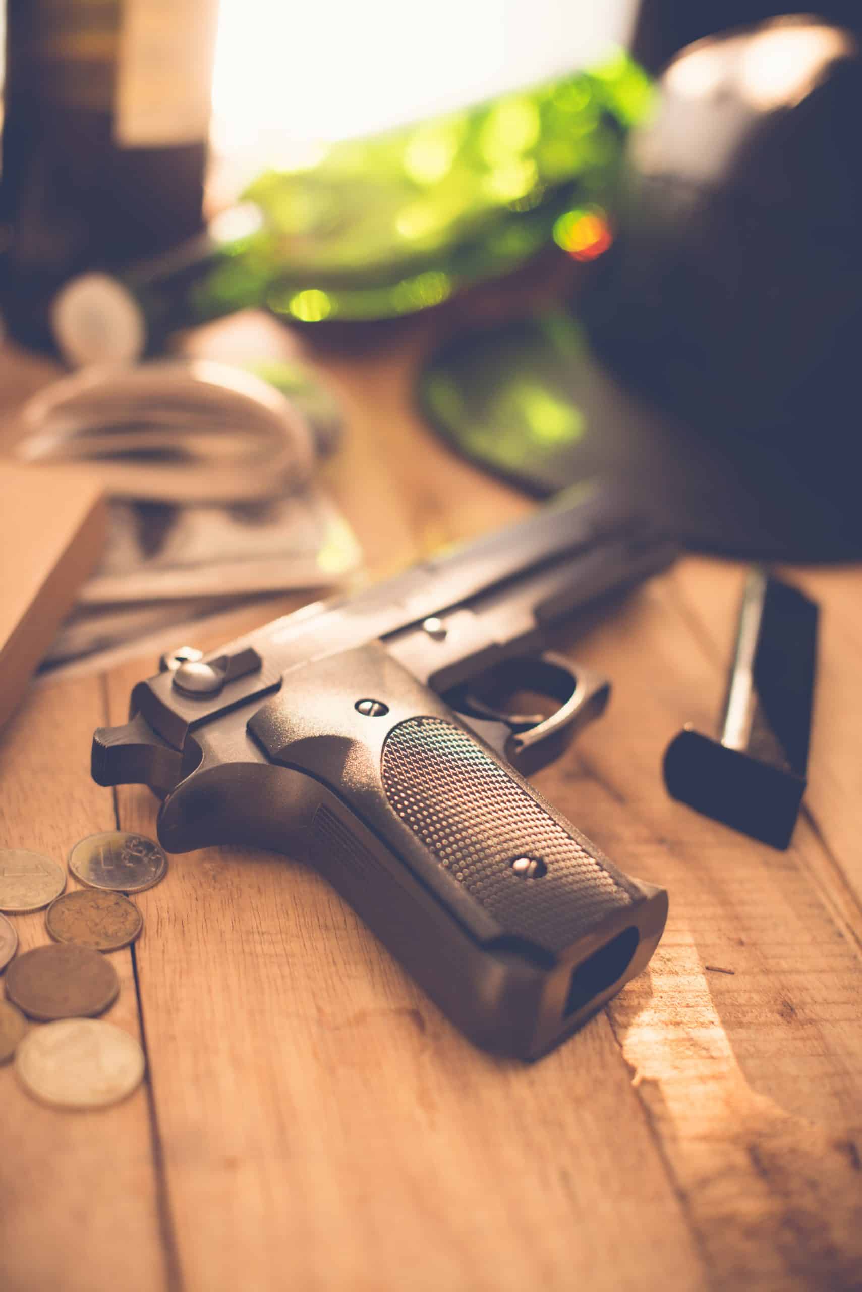 Pistol on wooden table with coins and bottle.