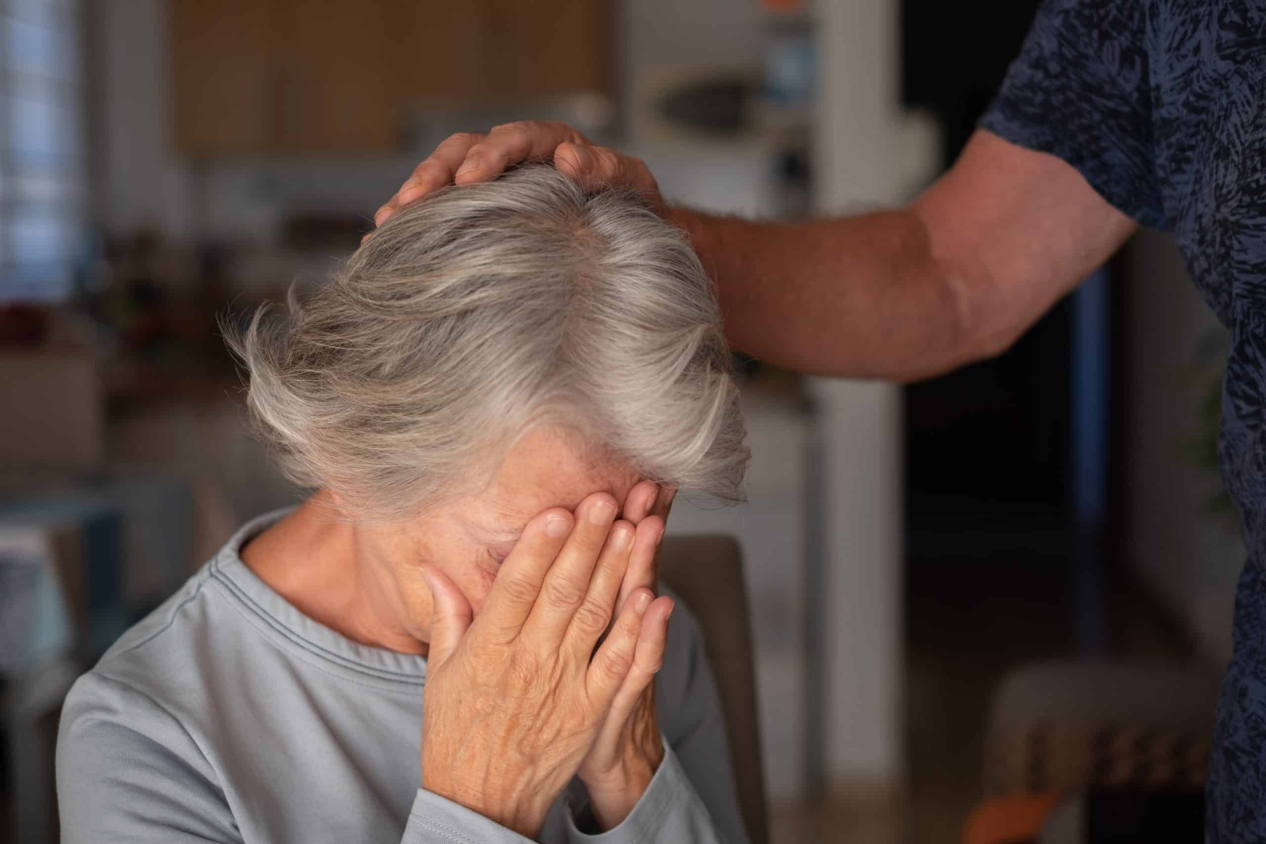Elderly woman comforted by another person.