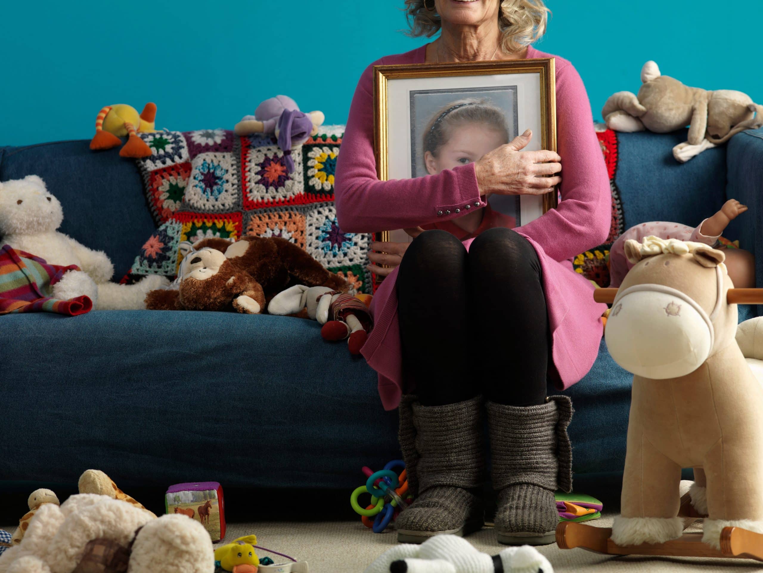 Woman holding child's photo surrounded by toys.